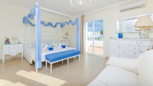 A bedroom with a four-poster bed, a chandelier, a white dresser, and a view of the outside. - SA CALETA - Villa with private pool in Cala Egos (Santanyi). Free WiFi (Santanyí)