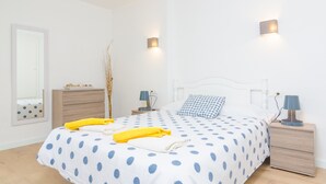 Une chambre à coucher comprenant un lit, des tables de chevet, une commode, une lampe, un miroir et une fenêtre donnant sur le ciel.