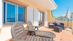 Une terrasse avec du mobilier d’extérieur, une vue sur la mer et un bâtiment doté d’un toit en tuiles.