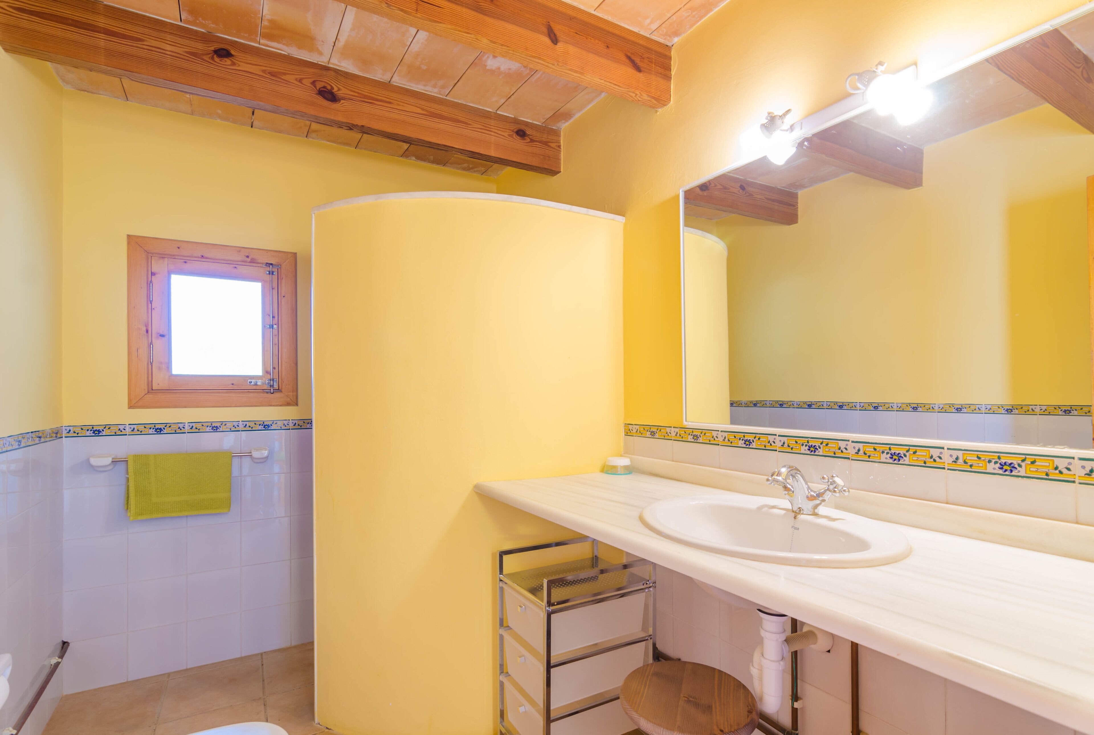 A bathroom with a white sink, wooden ceiling beams, a mirror, and a window.