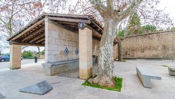 Un pavillon en pierre avec un toit en tuiles, des bancs et un arbre, situé sur une place publique.