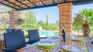 Un espace repas extérieur avec vue sur la piscine, des tables en bois et des chaises en osier.