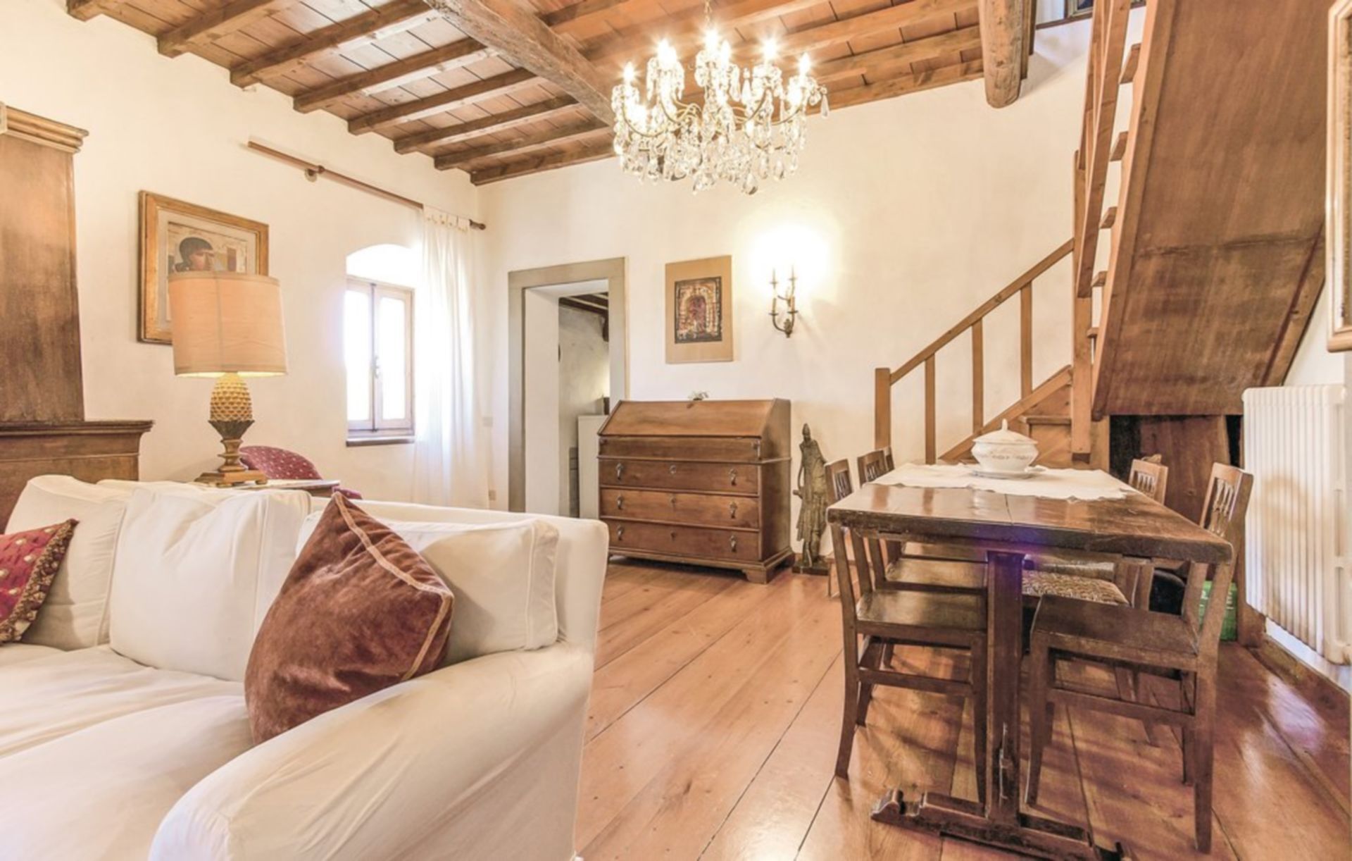 Um quarto aconchegante com teto de madeira, um lustre, uma mesa de jantar com cadeiras, um sofá com almofadas e um aparador.