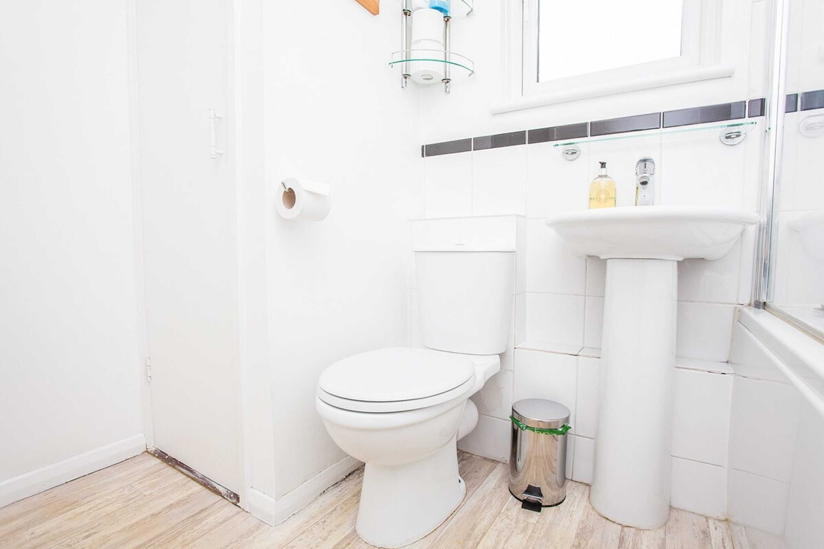 A small, white bathroom with a toilet, sink, and a trash bin.