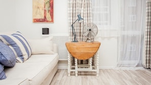 Quarto com sofá branco, mesa lateral de madeira com um ventilador, luminária e radiador.