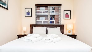 Cama bem arrumada com roupa de cama e toalhas brancas, cabeceira de madeira e duas luminárias de cabeceira.