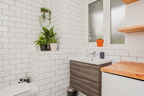 A bathroom with white tiled walls, a wooden countertop, a sink, and a window above the mirror.