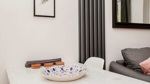 Un coin repas avec une table en marbre blanc, un bol aux motifs bleus et une œuvre d’art représentant une plume, encadrée, accrochée au mur.