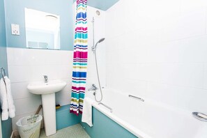Une salle de bain avec un lavabo, une douche et des toilettes. Il y a un rideau de douche rayé et coloré.