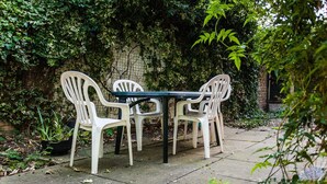 En terrasse med et bord og fire stole, omgivet af grøn vegetation og en murstensmur.