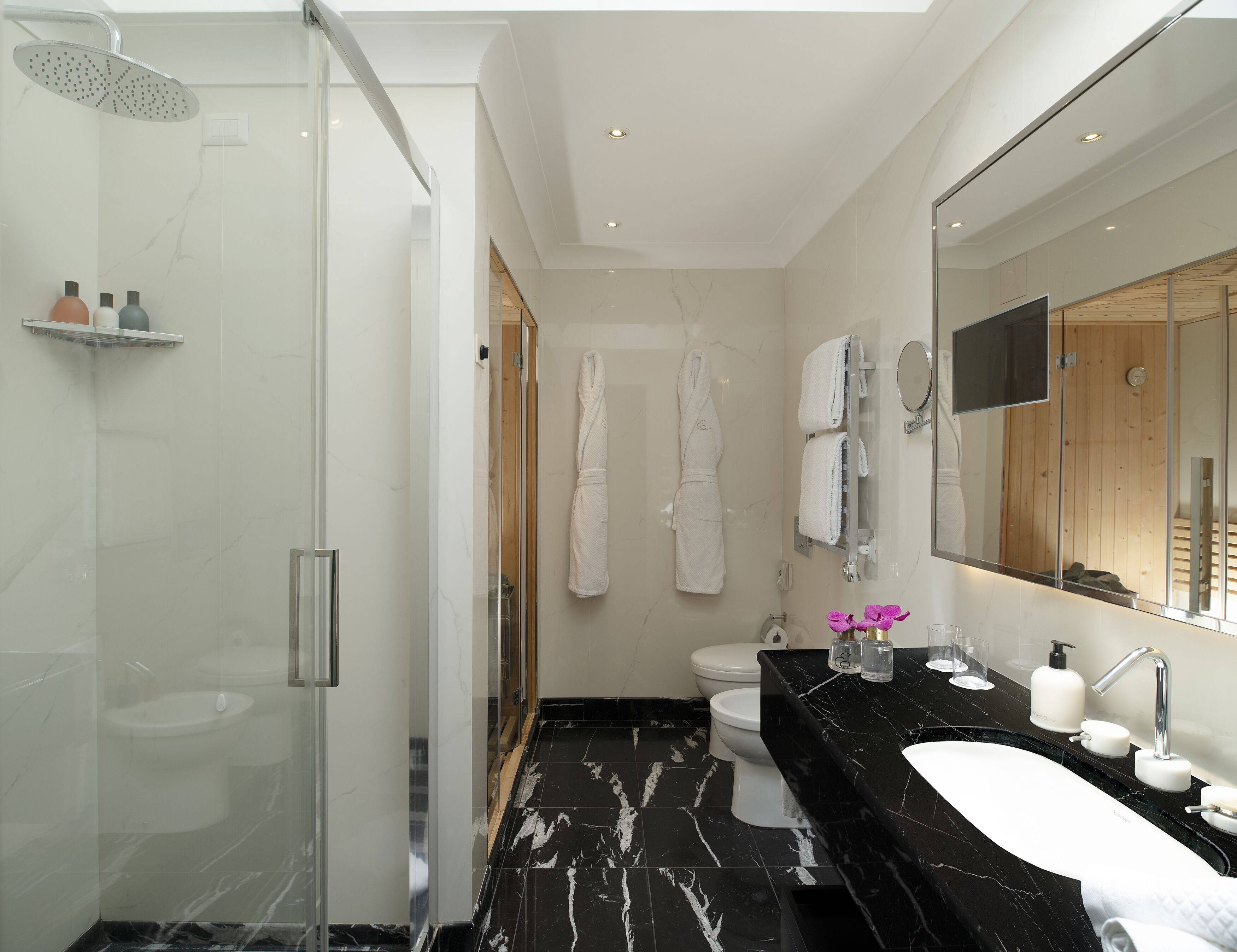 A modern bathroom with a glass-enclosed shower, a white toilet, a black marble sink, and a large mirror.