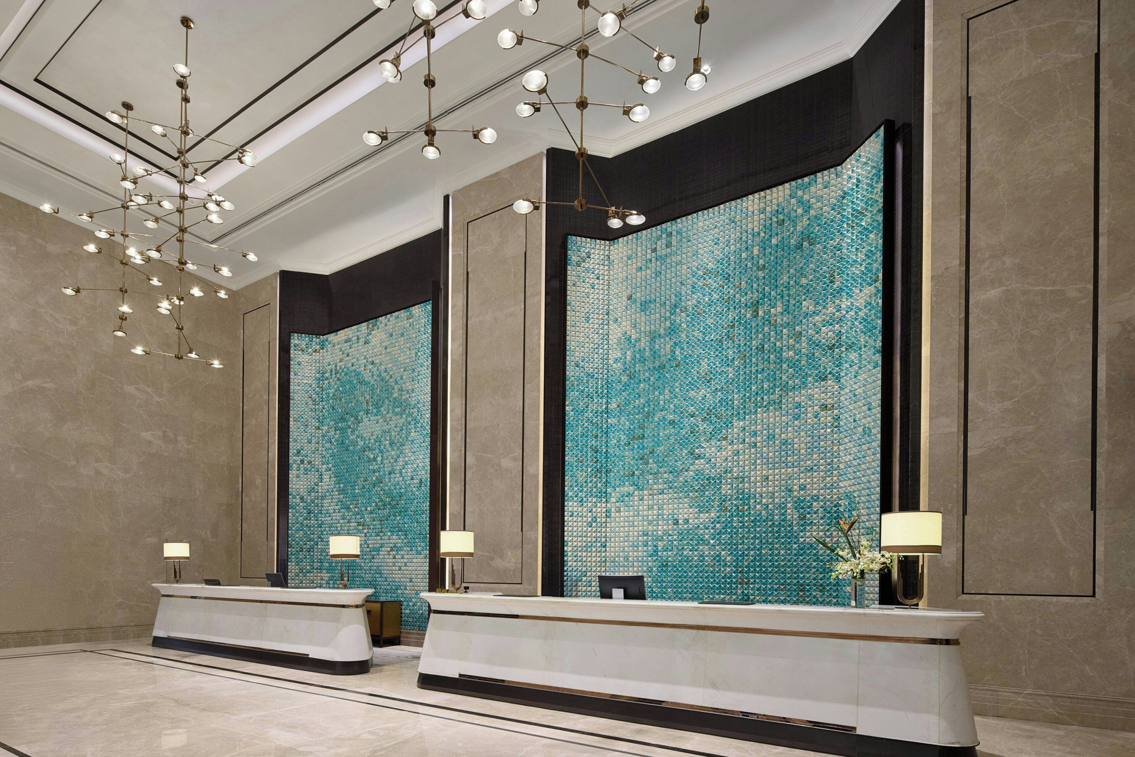 A modern reception area with a large mosaic wall, a reception desk, and a chandelier.