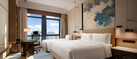 A hotel room with a large bed, a desk, a chair, and a view of the city through the window.