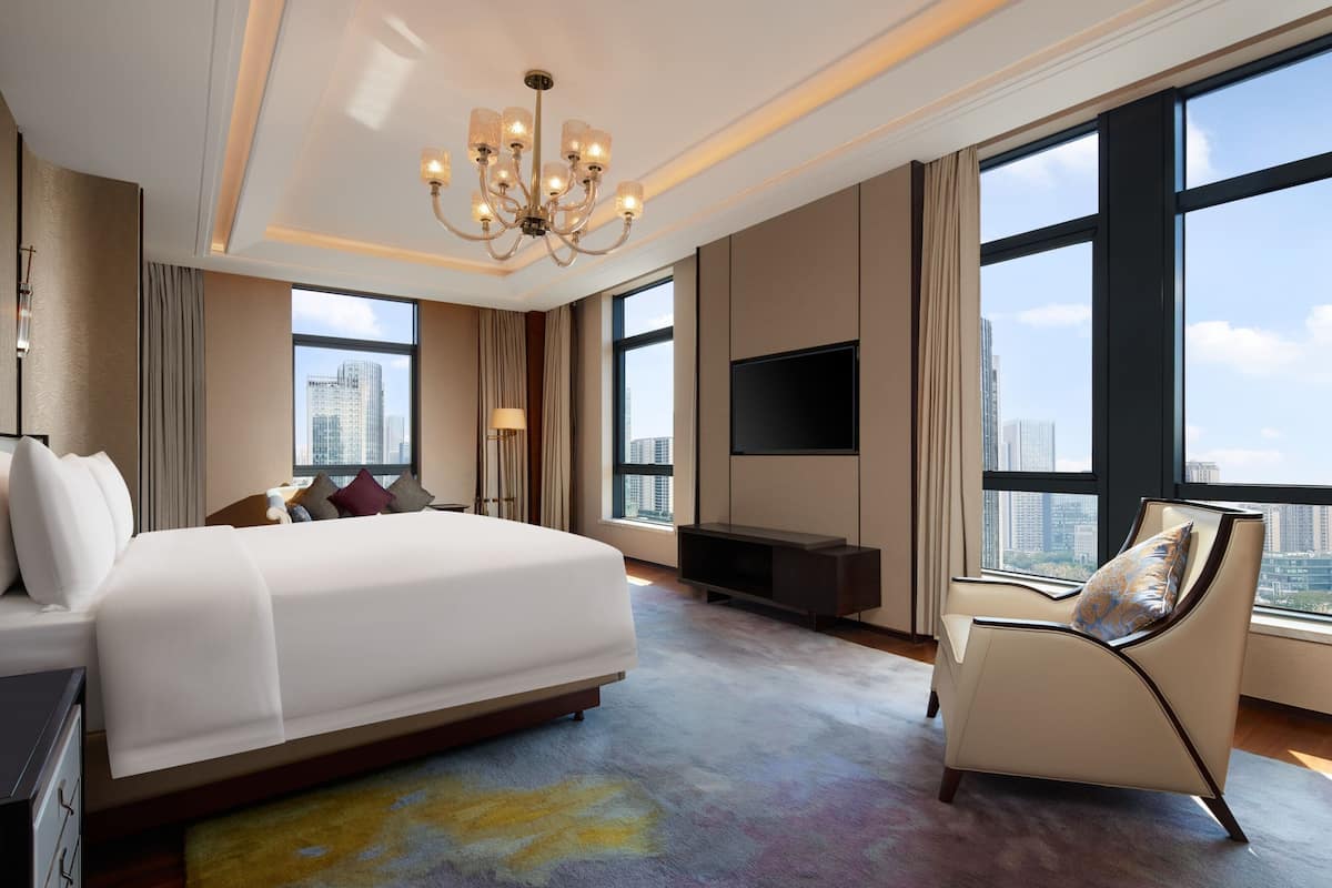 A modern hotel room with a large bed, a seating area, a flat-screen TV, and a city view.