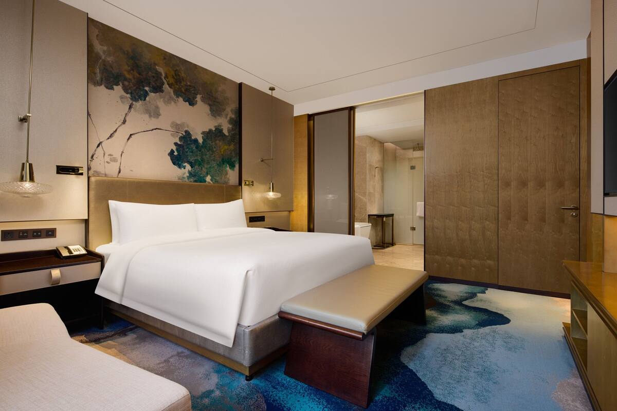 A modern hotel room with a large bed, a bench, a desk, and a walk-in closet.