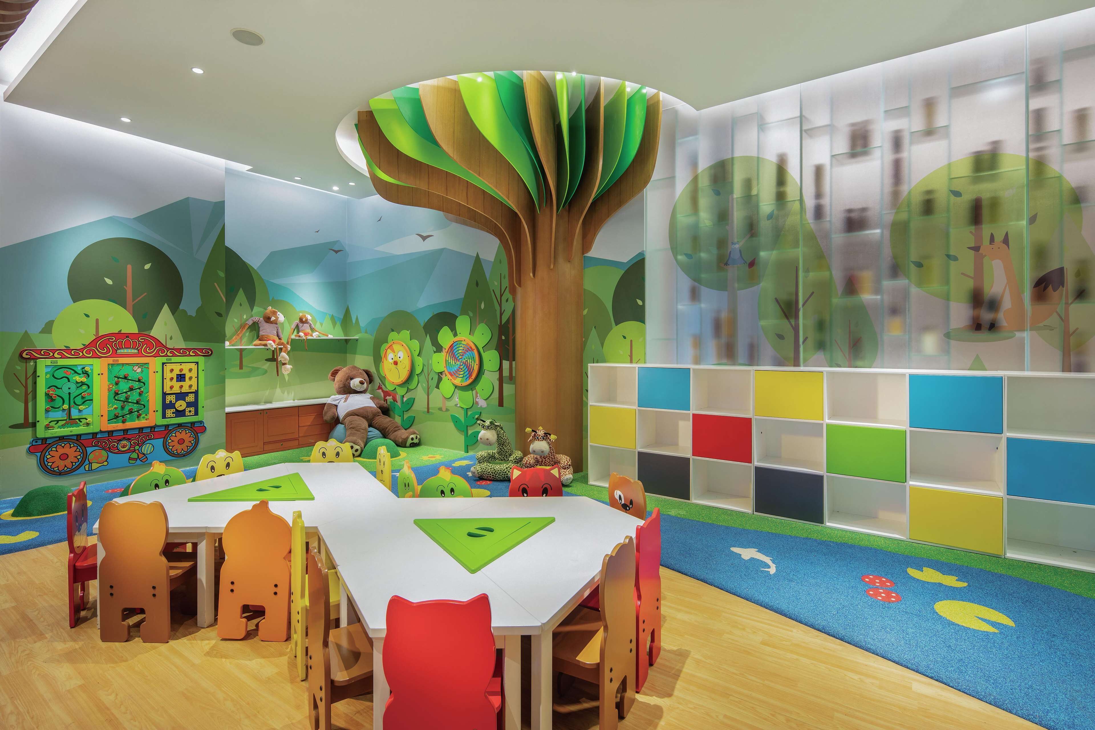 A children's play area with a large tree mural, a play table, and colorful storage units.