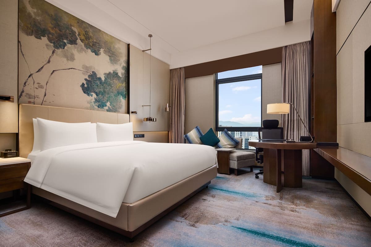 A modern hotel room with a large bed, a desk, and a view of the city.