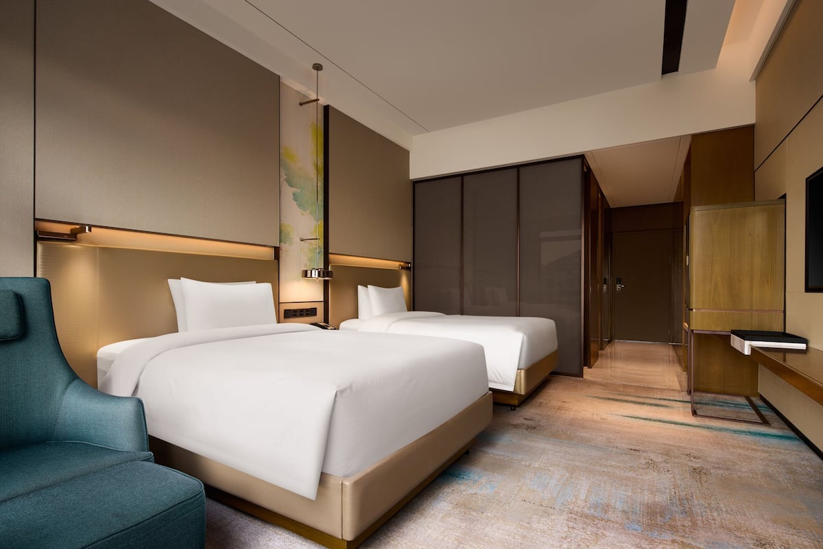 A modern hotel room with two beds, a seating area, and a large wardrobe.
