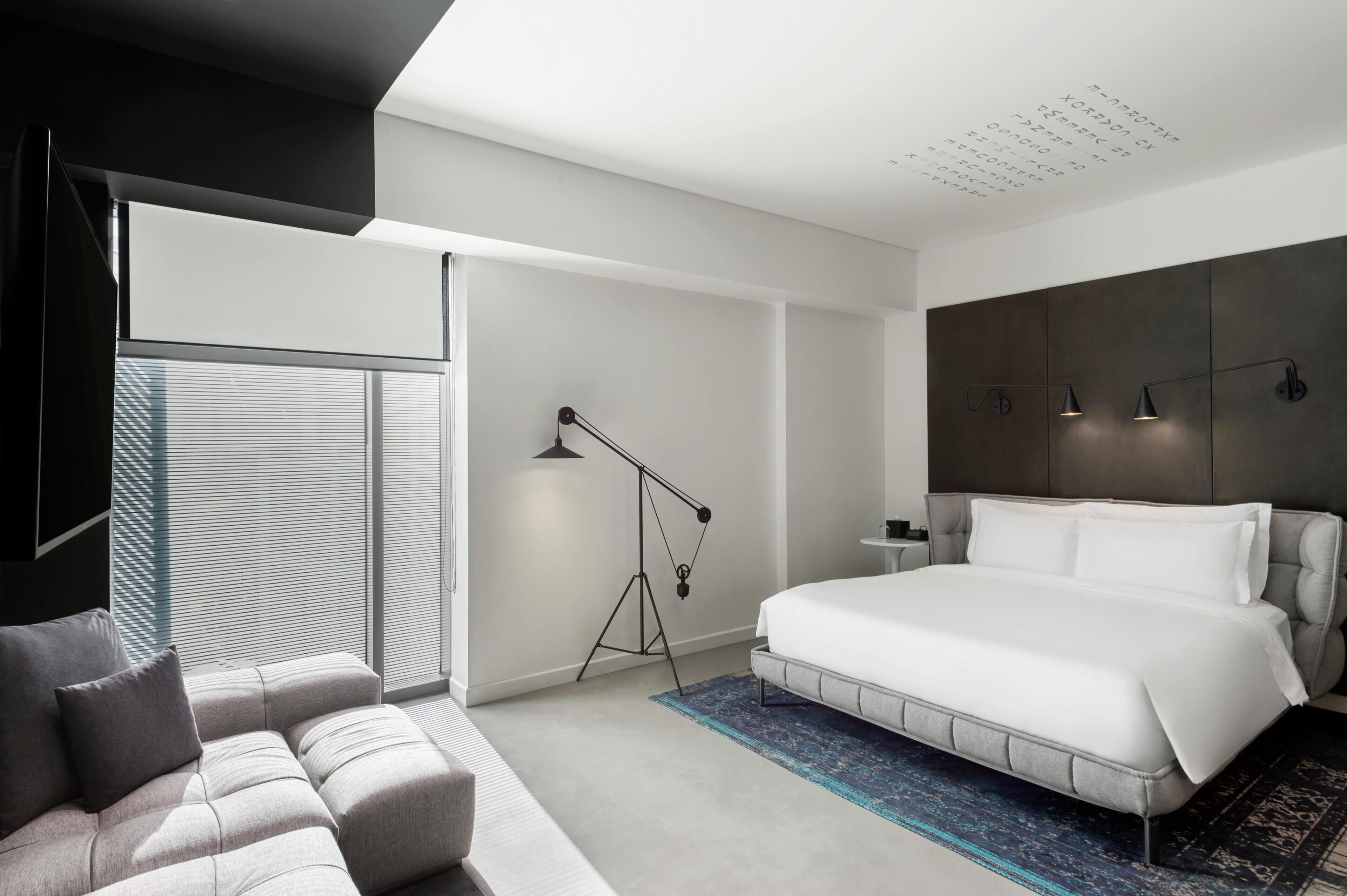 Un dormitorio moderno con una cama grande, un sofá, una lámpara de pie y vistas al exterior.