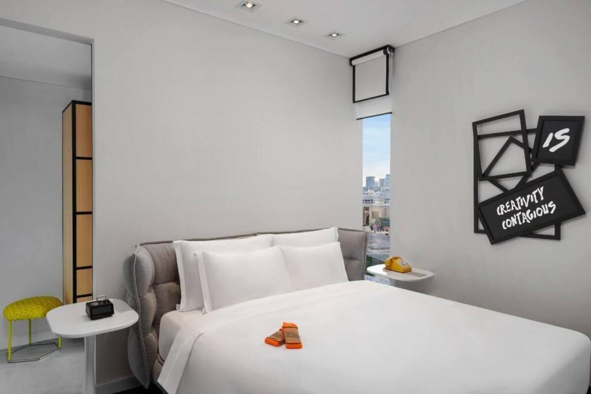 A modern hotel room with a bed, a small table, a chair, and a city view.