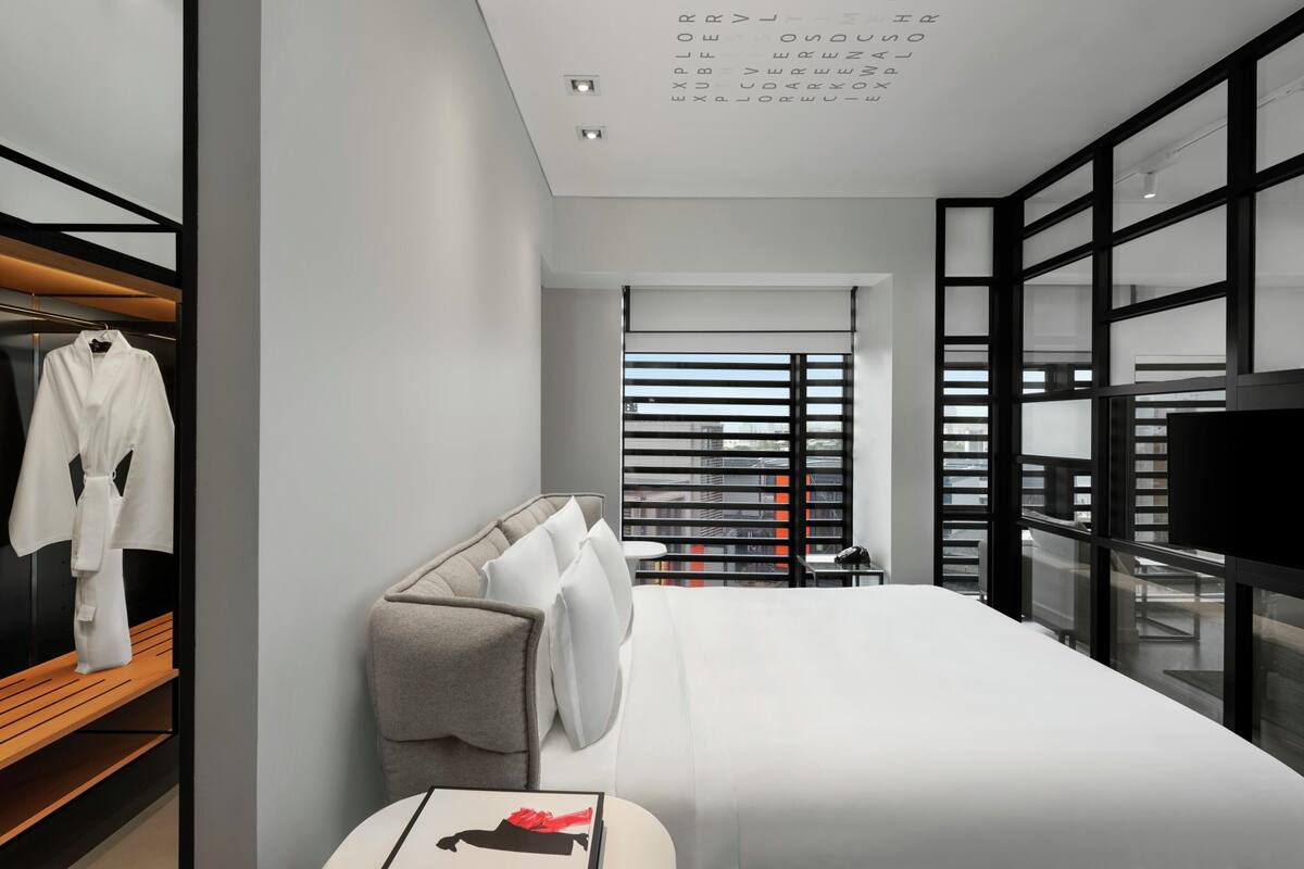A modern hotel room with a large bed, a bedside table, a TV, and a wardrobe.
