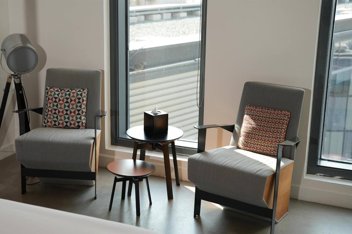 A modern room with two grey armchairs, a small round table, and a floor lamp.