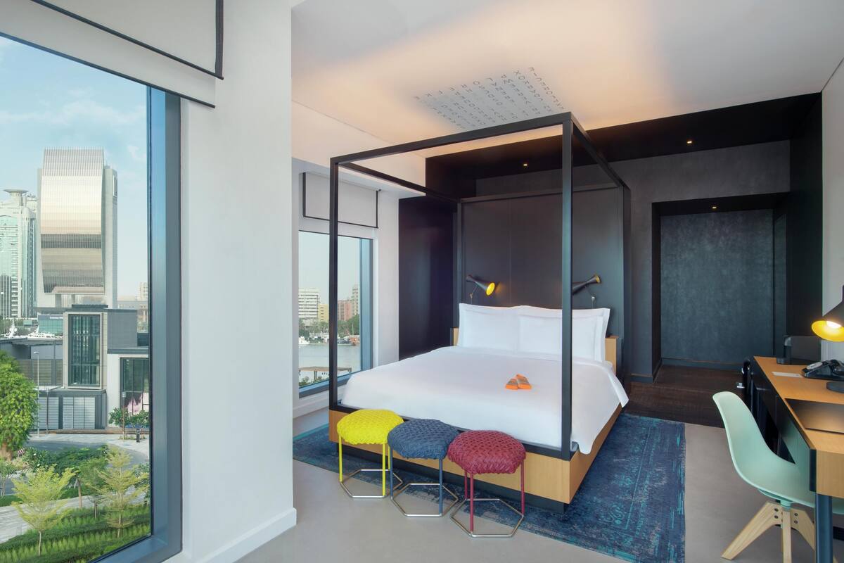 A modern hotel room with a large bed, a desk, and a view of the cityscape.