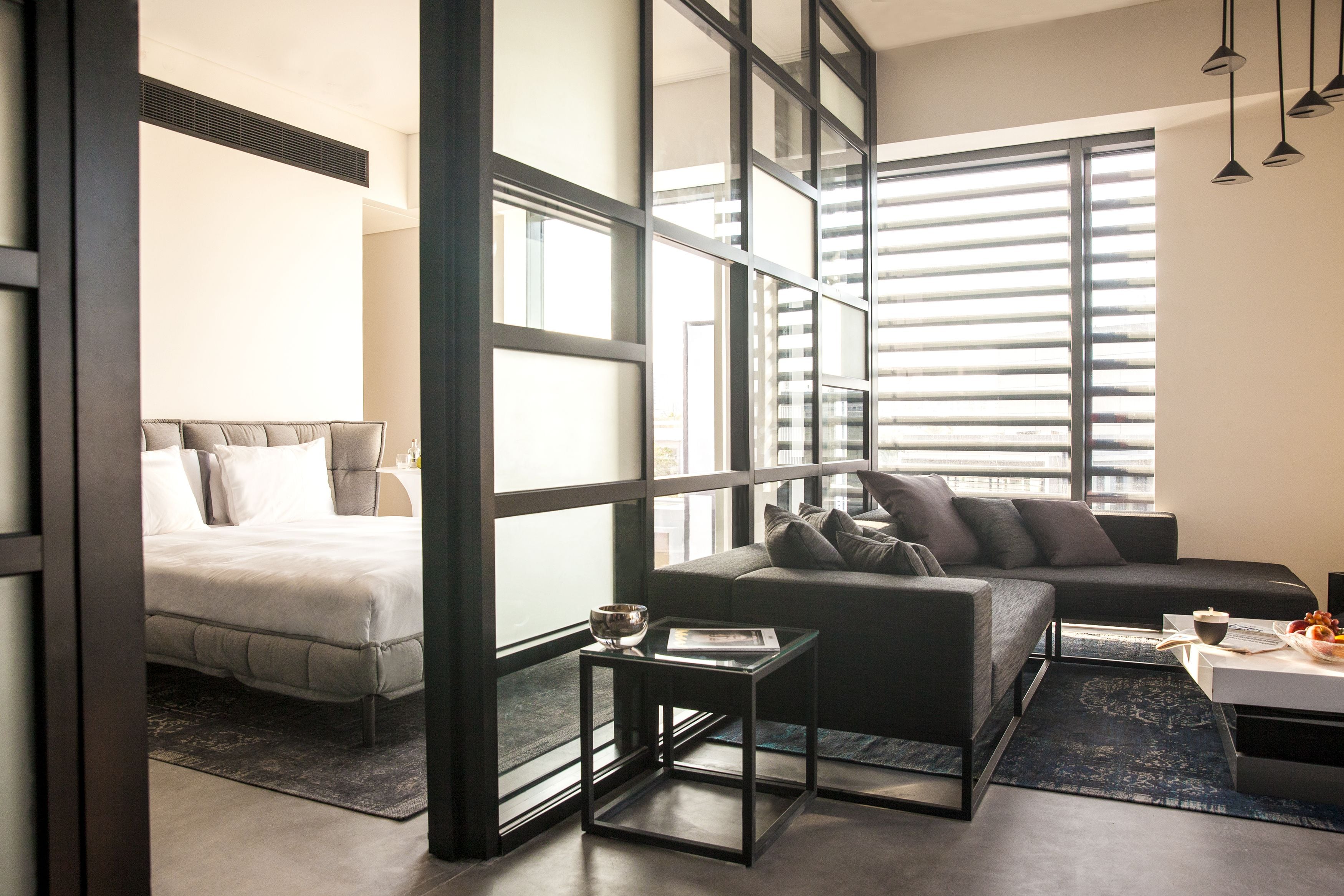 A modern hotel room with a bed, a sofa, a coffee table, and large windows.