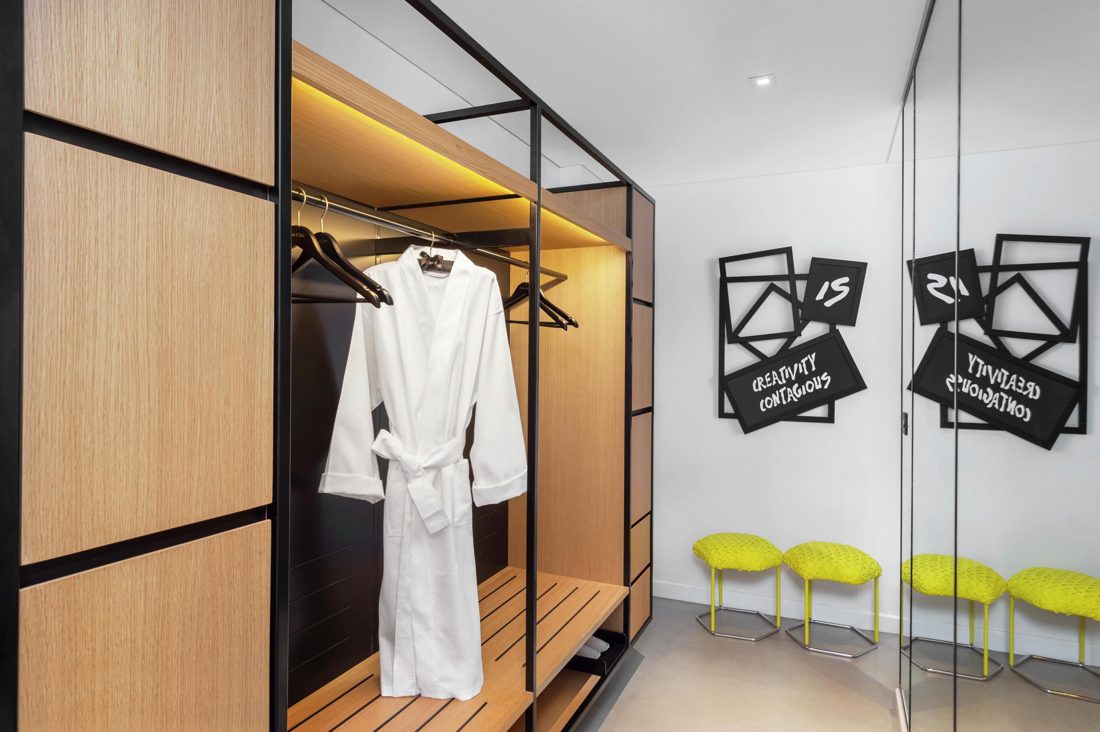 Een moderne hotelkamer met een houten kast, een witte badjas en een spiegel met geometrische wanddecoratie.