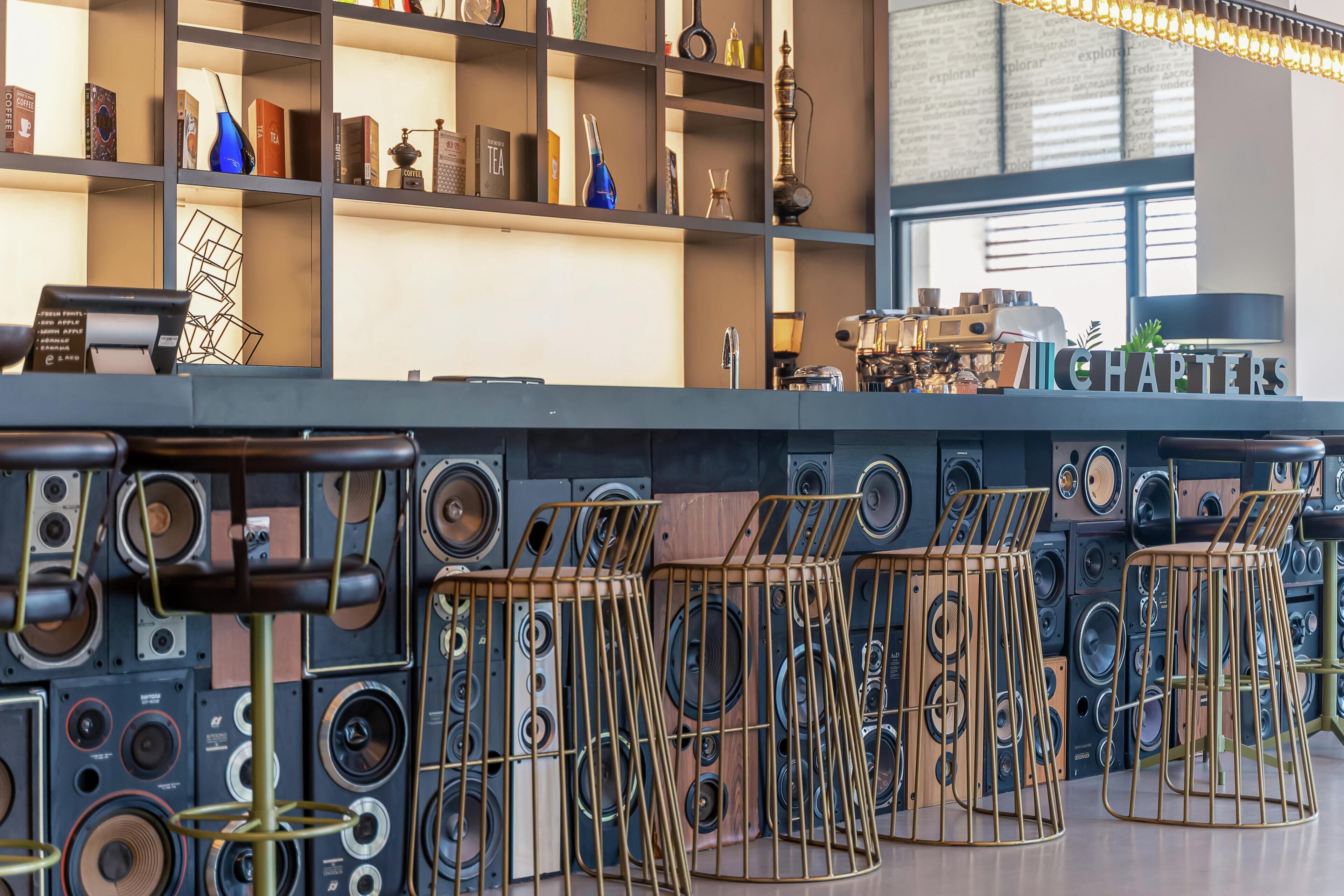 Eine Bar mit mehreren Lautsprechern und Hockern, einer Kaffeemaschine und Regalen mit verschiedenen Gegenständen.