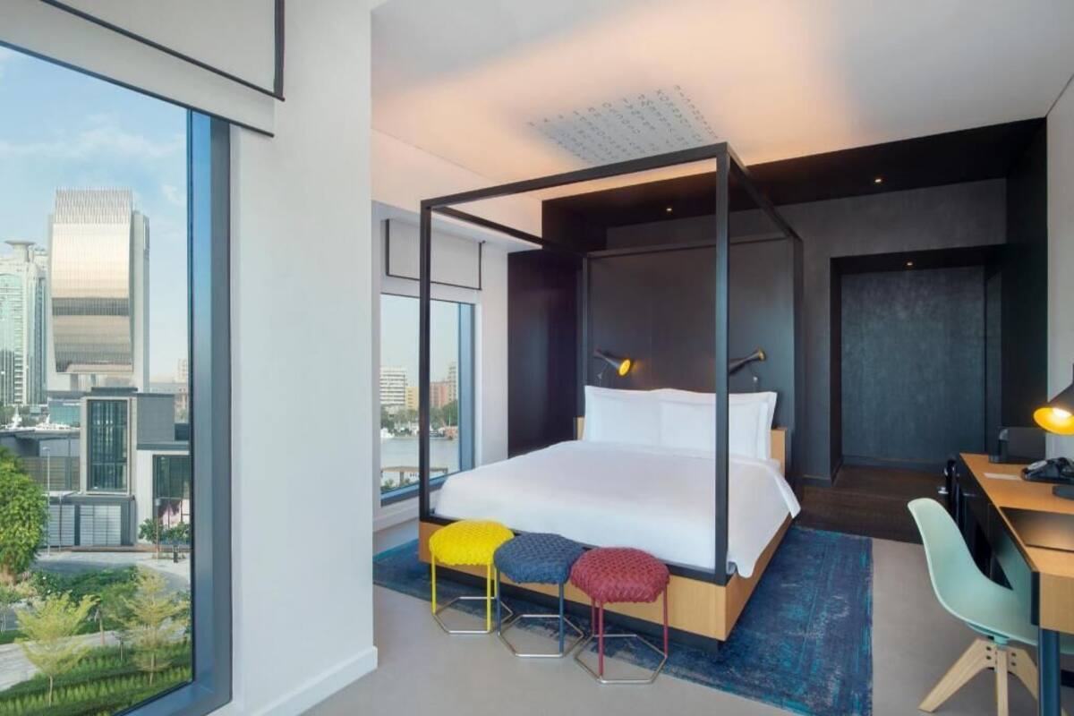 A modern hotel room with a large bed, a desk, and a view of the cityscape.