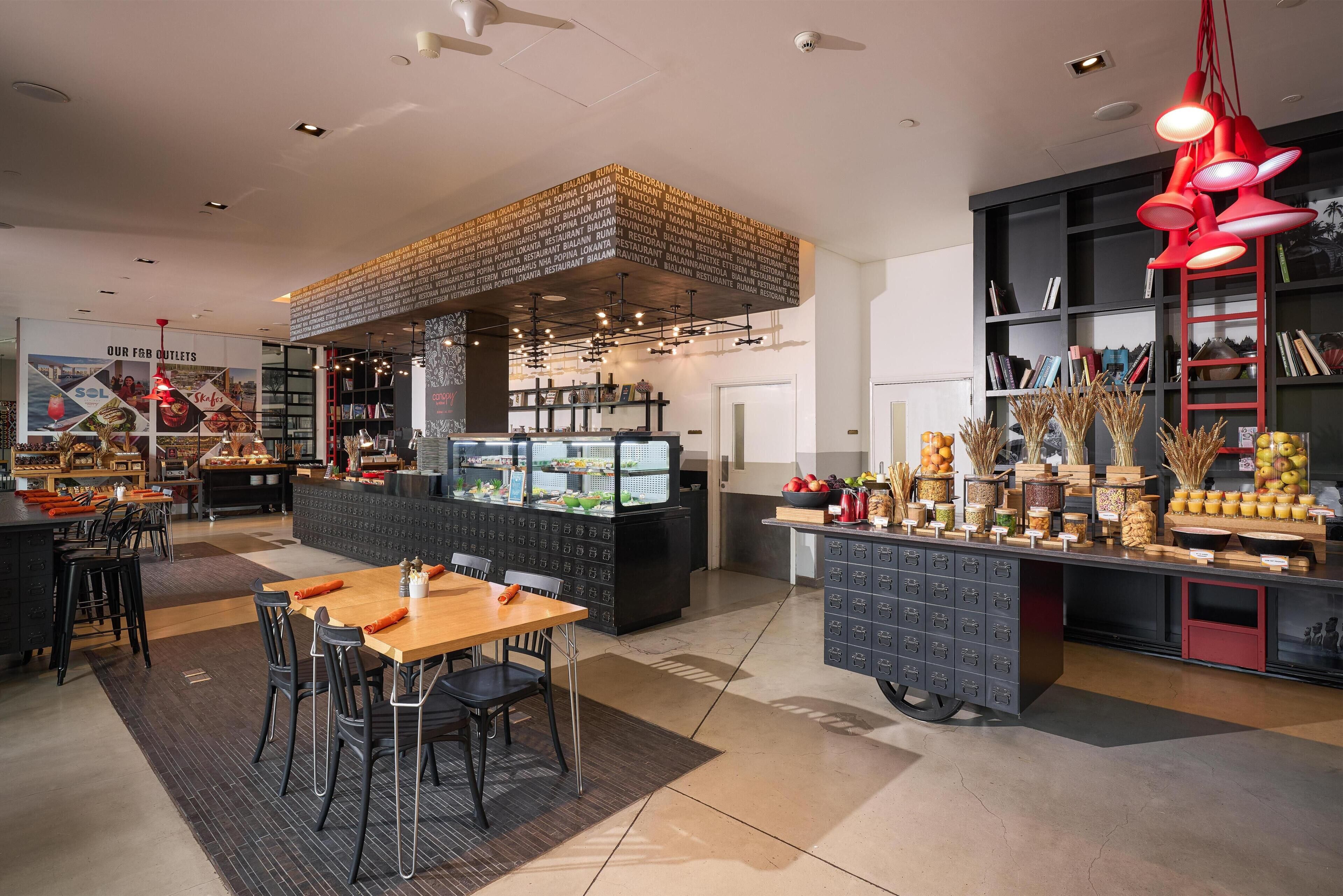 Interior moderno de restaurante con barra central, distribución de mesas y exhibición de alimentos.