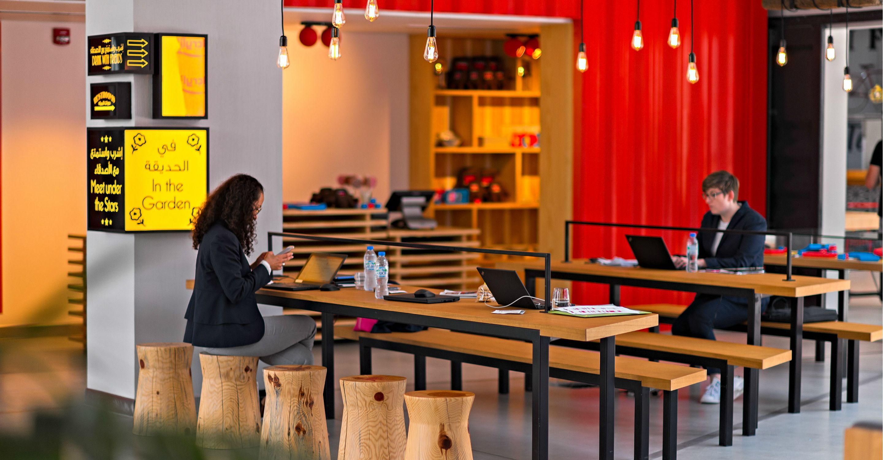 A modern co-working space with wooden tables and benches, laptops, and a red accent wall.