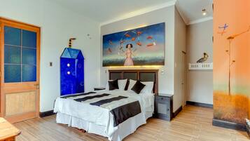 Une chambre à coucher avec un grand lit, un tableau représentant une femme et des poissons, une porte en bois et une table de chevet.