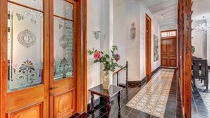Un pasillo con puertas de madera, piso de baldosas y un jarrón con flores sobre una mesa.