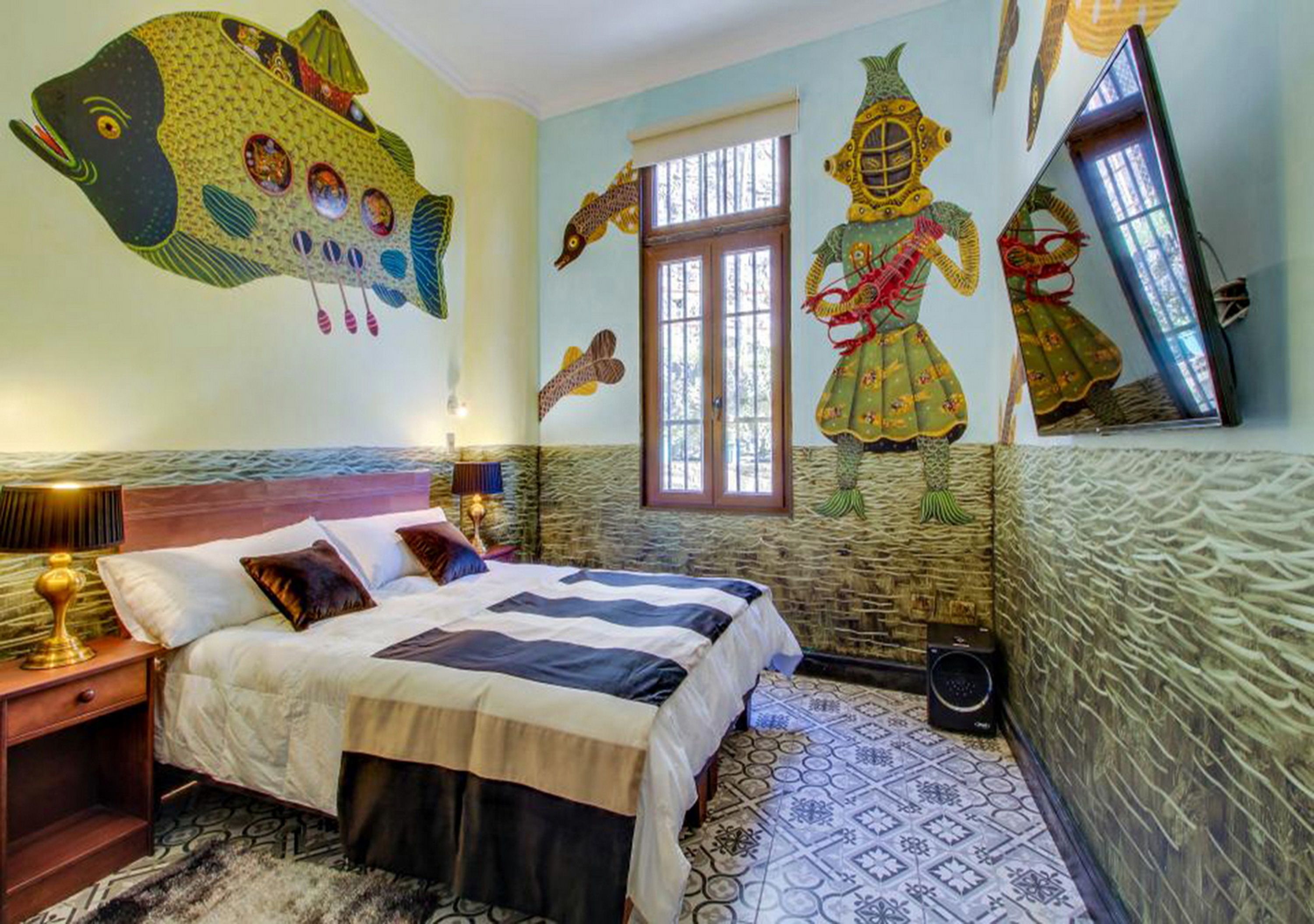 Una habitación con una cama, una mesita de noche, una lámpara, una ventana y una pared decorada con motivos marinos y criaturas marinas.
