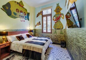Una habitación con una cama, una mesita de noche, una lámpara, una ventana y una pared decorada con motivos marinos y criaturas marinas.