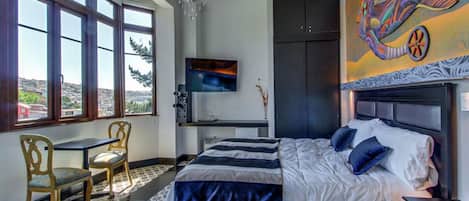 A bedroom with a bed, a desk, and a TV. There are windows and a view of the outside.