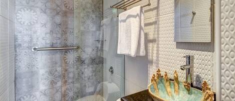 Un baño con ducha de vidrio, lavamanos decorativo y un perchero para toallas.