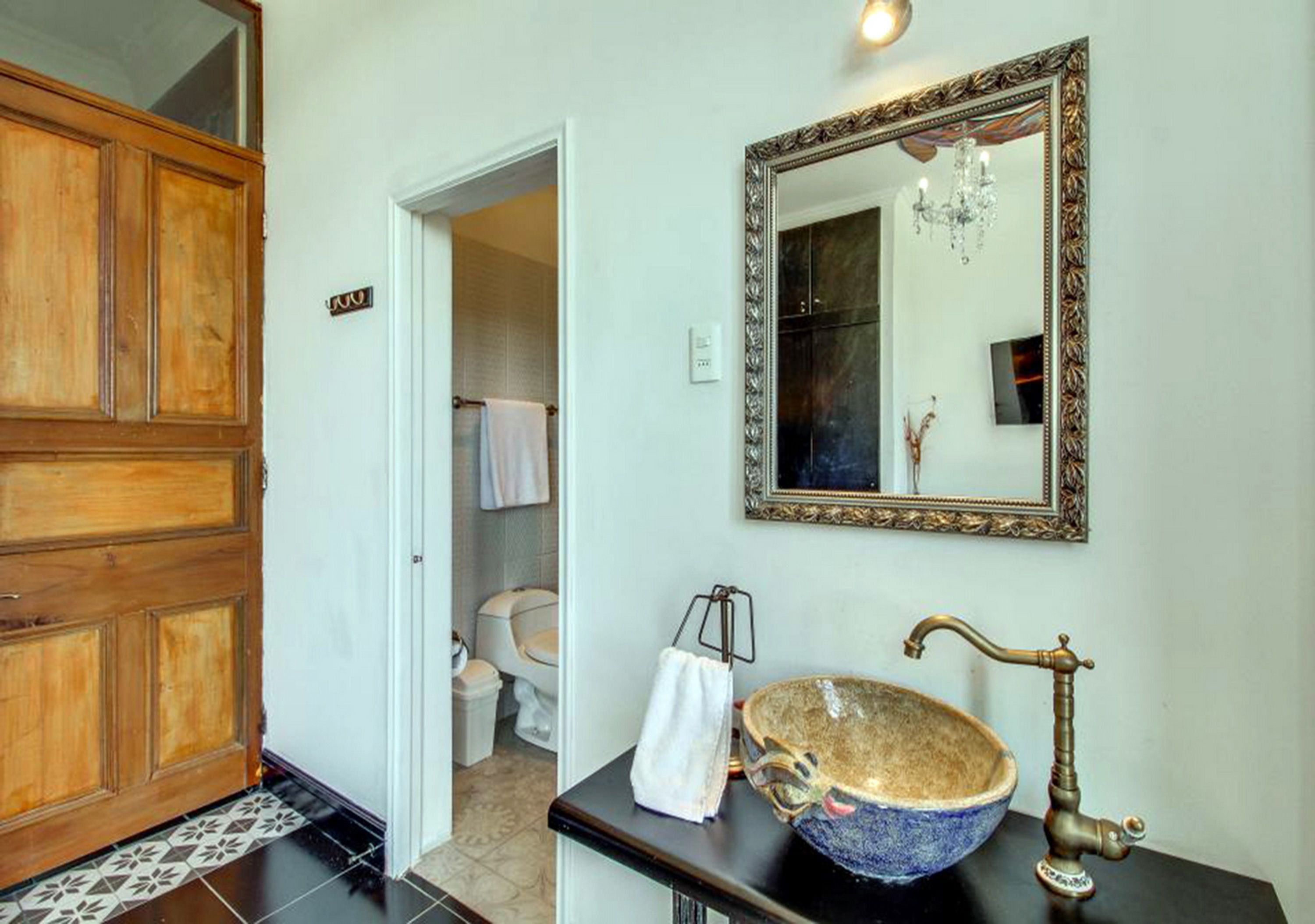 A bathroom with a wooden door, a large mirror, a vintage-style sink, and a chandelier.