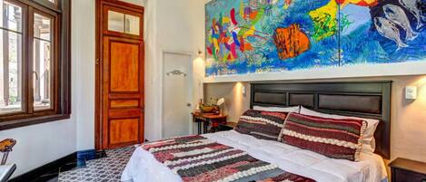 A bedroom with a large bed, a colorful abstract painting above the bed, and a patterned floor.