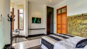 Un dormitorio con cama, televisor, armario y un cuadro en la pared.