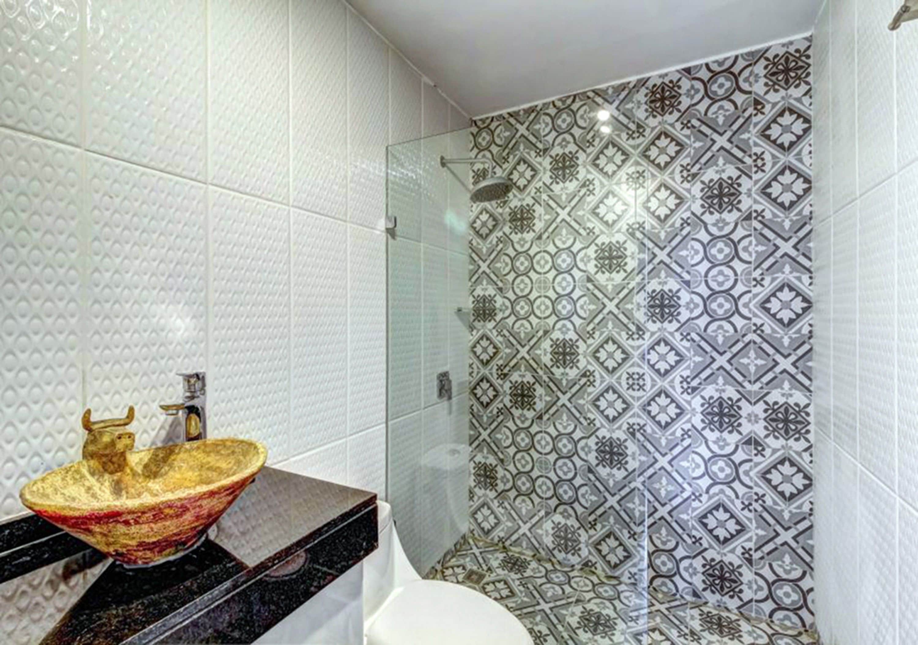 A bathroom with a large, ornate gold bowl sink, a shower with patterned tiles, and a white toilet.