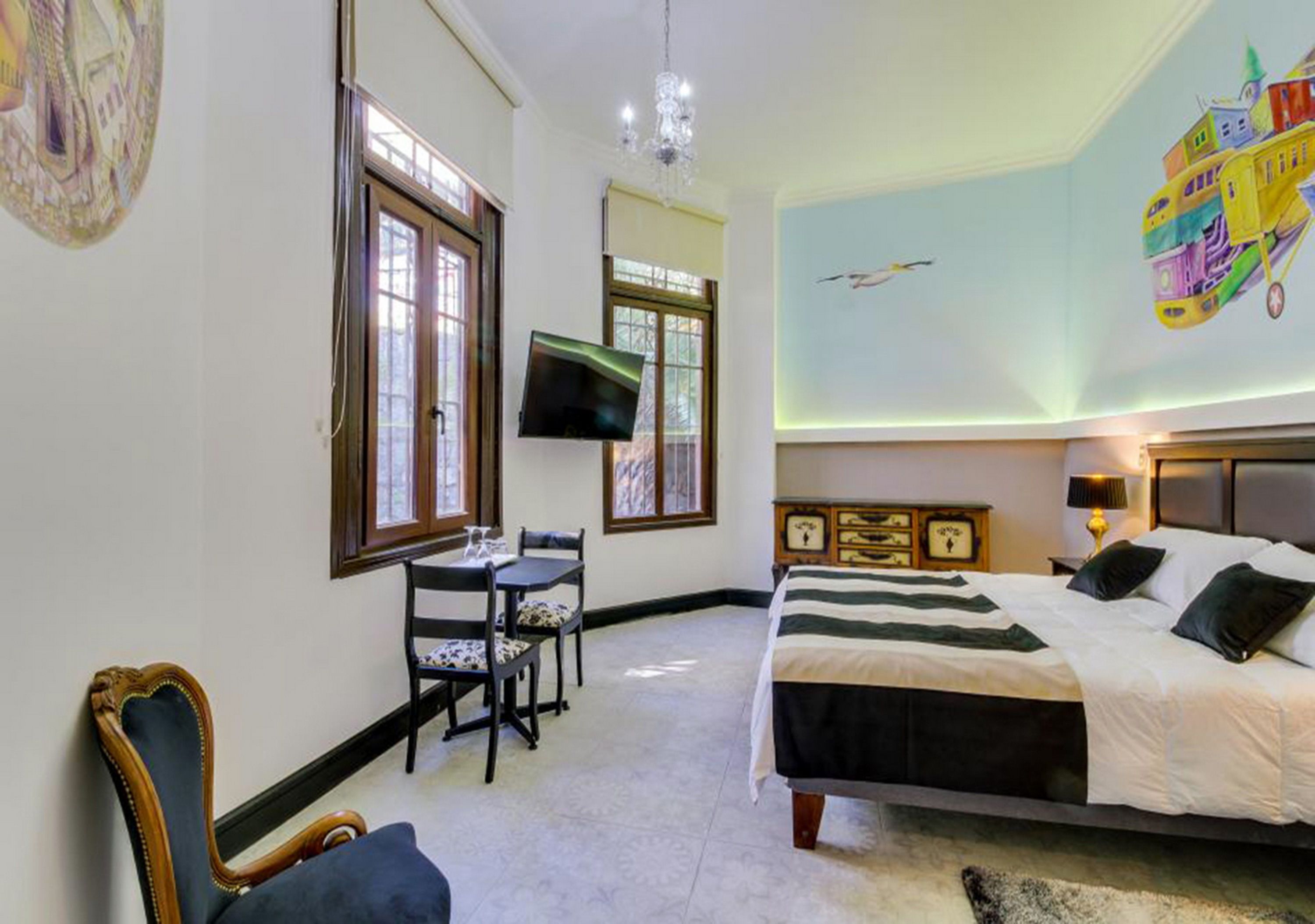 A hotel room with a bed, a desk, a chair, a television, and a wall with a mural.
