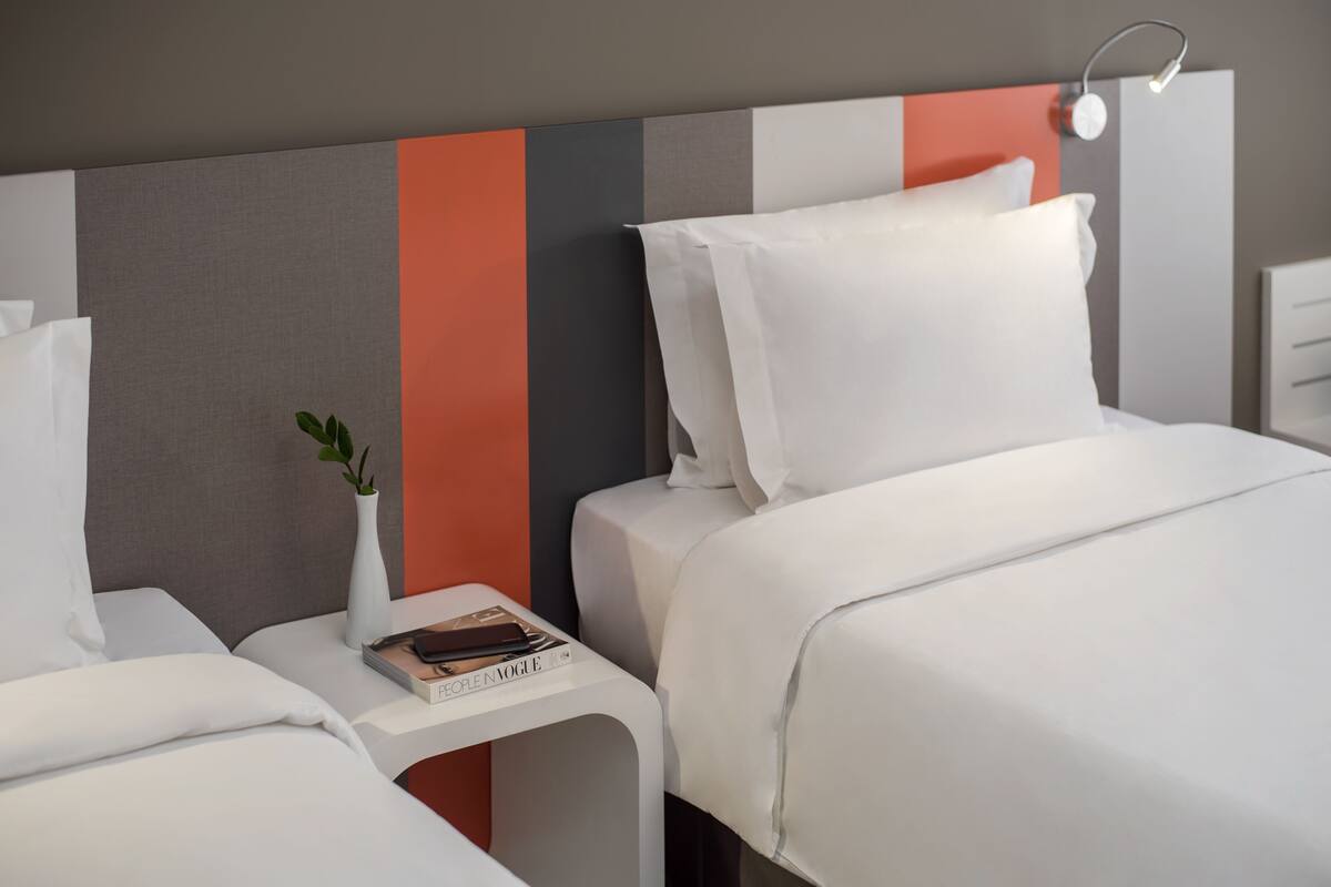A hotel room with a bed, bedside tables, a nightstand, and a wall with a striped pattern.