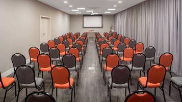 Un salón de conferencias con filas de sillas, una pantalla de proyector y un atril.