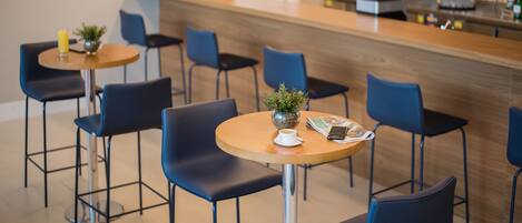 Un café moderno con mesas redondas y sillas azules, una barra de madera con una computadora portátil y una planta en maceta.