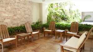 A patio area with wooden chairs and a table, surrounded by a brick wall and lush greenery. - Charming 3 Bedroom in the Old City (Cartagena)