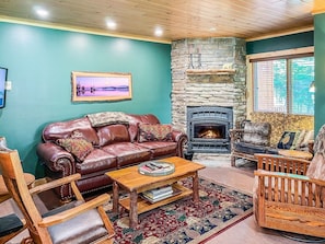 A cozy living room with a stone fireplace, leather sofa, and a patterned rug.