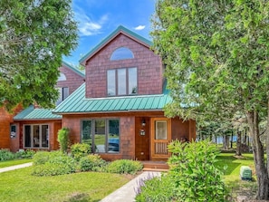 A two-story house with a green roof, a front porch, and a well-maintained lawn.